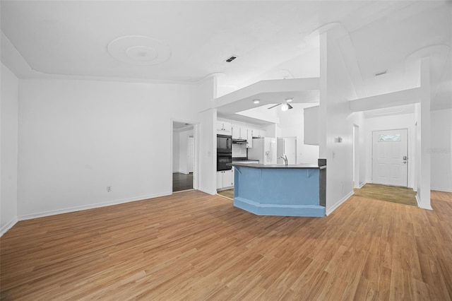 unfurnished living room with light hardwood / wood-style floors, high vaulted ceiling, ceiling fan, and sink