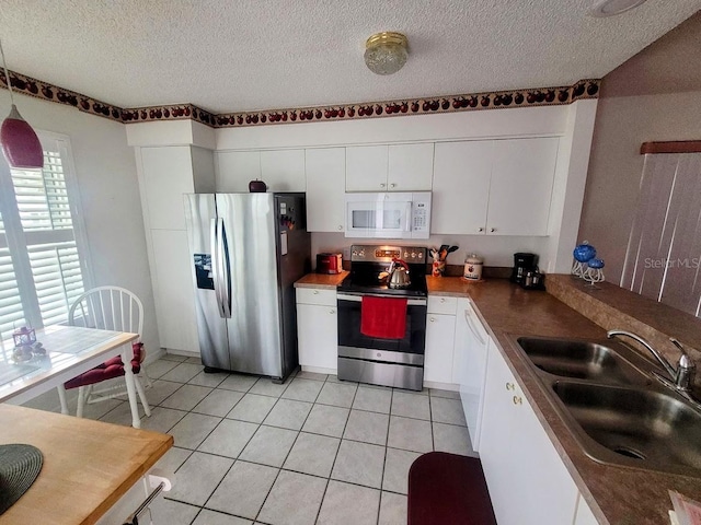 kitchen featuring appliances with stainless steel finishes, light tile patterned floors, a textured ceiling, white cabinetry, and sink