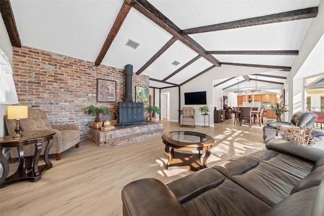 living room with lofted ceiling with beams, light wood-type flooring, brick wall, and a wood stove