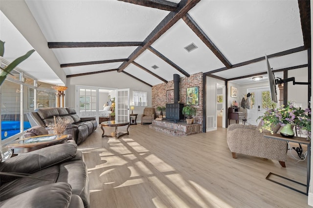 living room featuring a wood stove, vaulted ceiling with beams, french doors, and light wood-type flooring