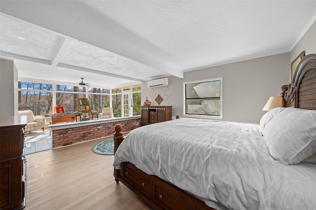 bedroom with a textured ceiling, a wall unit AC, beamed ceiling, and light wood-type flooring