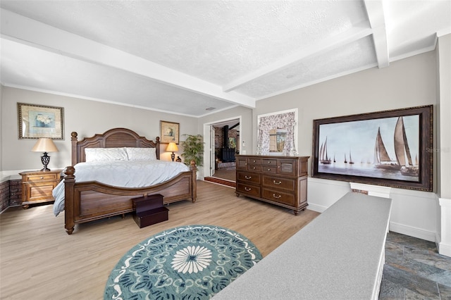 bedroom featuring a textured ceiling, light hardwood / wood-style floors, and beamed ceiling