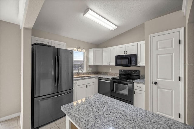 kitchen with light stone counters, black appliances, lofted ceiling, white cabinetry, and sink