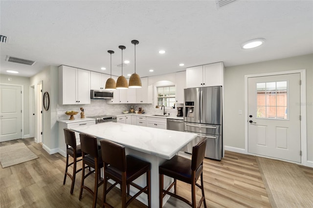 kitchen featuring white cabinets, a kitchen island, decorative light fixtures, stainless steel appliances, and sink