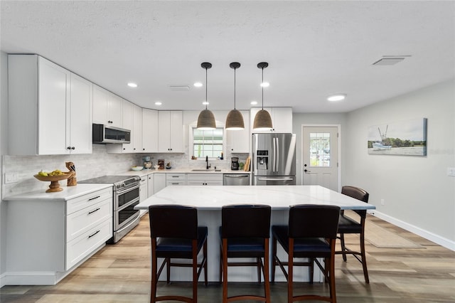 kitchen featuring a kitchen island, sink, hanging light fixtures, stainless steel appliances, and white cabinets