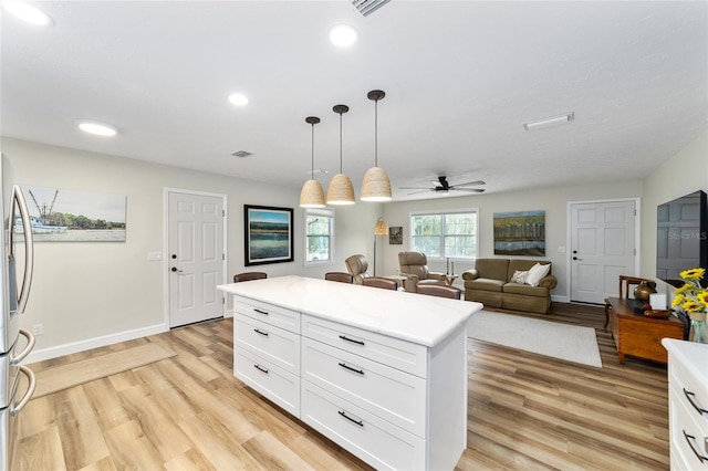 kitchen with ceiling fan, decorative light fixtures, a kitchen island, light hardwood / wood-style floors, and white cabinets