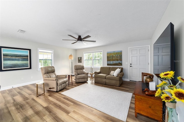 living room featuring ceiling fan, light wood-type flooring, and a textured ceiling