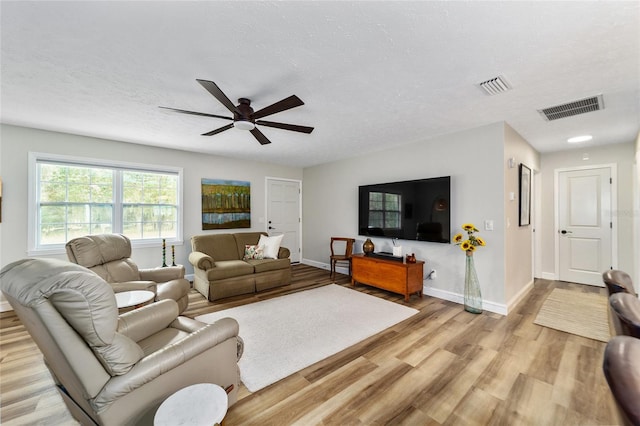 living room with light hardwood / wood-style floors, a textured ceiling, and ceiling fan