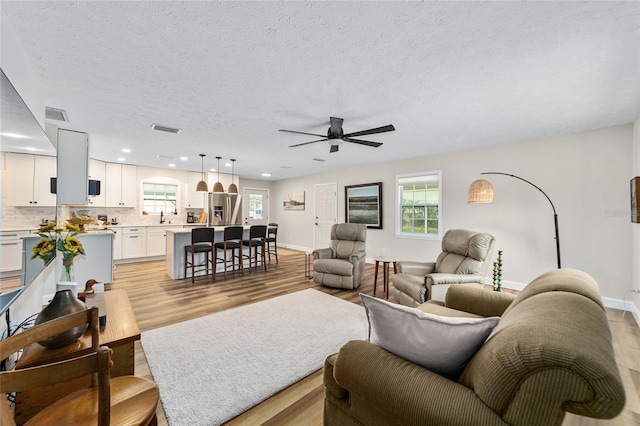 living room featuring ceiling fan, light hardwood / wood-style floors, a textured ceiling, and sink