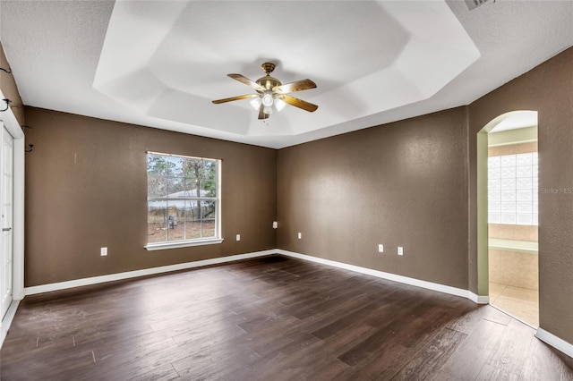 empty room featuring dark hardwood / wood-style flooring, ceiling fan, and a tray ceiling