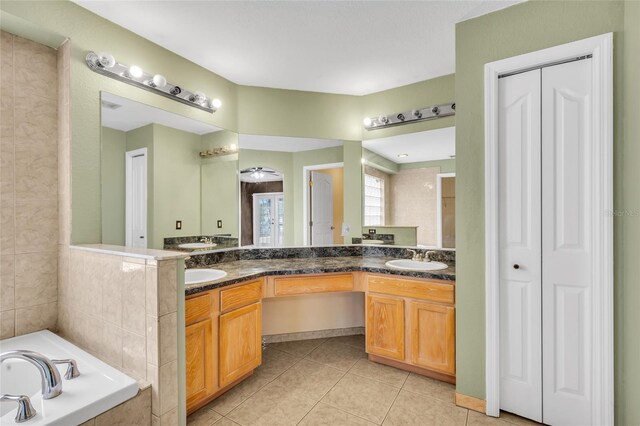 bathroom featuring tile patterned flooring, ceiling fan, a relaxing tiled tub, and vanity