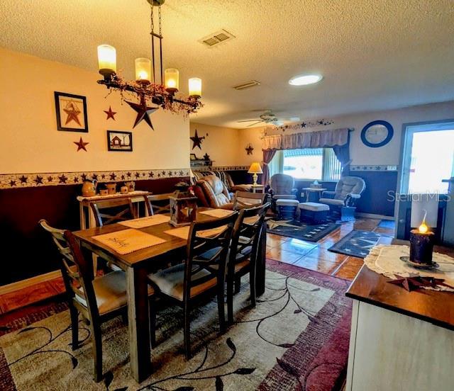 tiled dining area featuring ceiling fan with notable chandelier and a textured ceiling