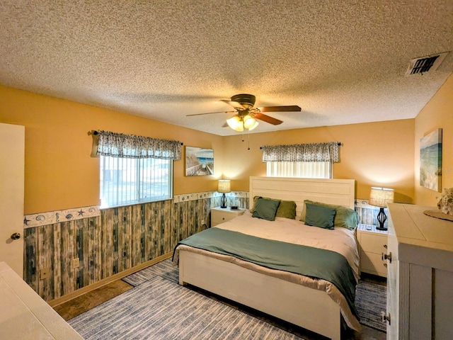 bedroom with a textured ceiling, wooden walls, and ceiling fan