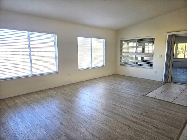 unfurnished room with vaulted ceiling, hardwood / wood-style floors, and a wealth of natural light