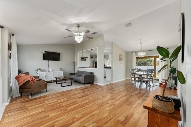 living room featuring lofted ceiling, ceiling fan with notable chandelier, and light wood-type flooring