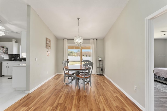 dining room with vaulted ceiling, ceiling fan with notable chandelier, and light wood-type flooring