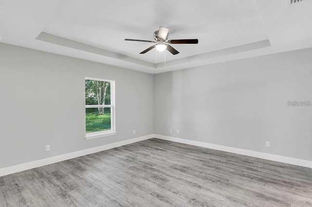 empty room with ceiling fan, light hardwood / wood-style flooring, and a raised ceiling