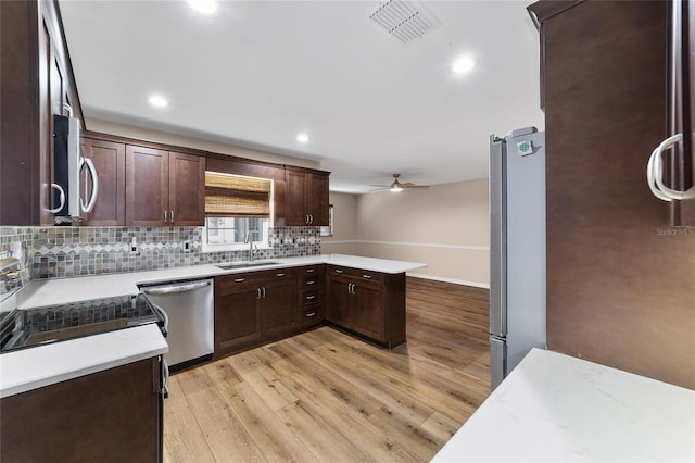 kitchen with appliances with stainless steel finishes, sink, kitchen peninsula, light wood-type flooring, and ceiling fan