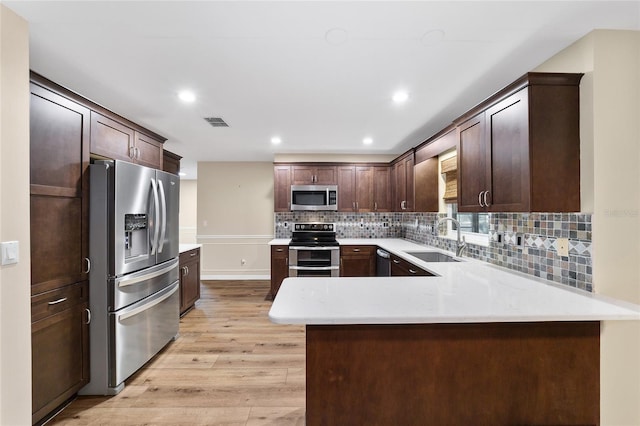 kitchen featuring kitchen peninsula, stainless steel appliances, light hardwood / wood-style flooring, dark brown cabinetry, and sink