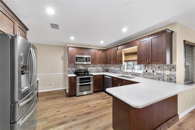 kitchen with stainless steel appliances, light hardwood / wood-style floors, sink, kitchen peninsula, and a breakfast bar area