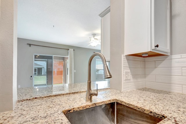 interior details with light stone countertops, white cabinets, tasteful backsplash, sink, and ceiling fan