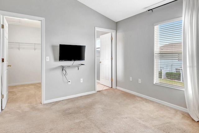 unfurnished bedroom with a closet, a walk in closet, lofted ceiling, and light colored carpet