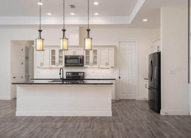 kitchen with white cabinetry, decorative light fixtures, black refrigerator, and a center island with sink