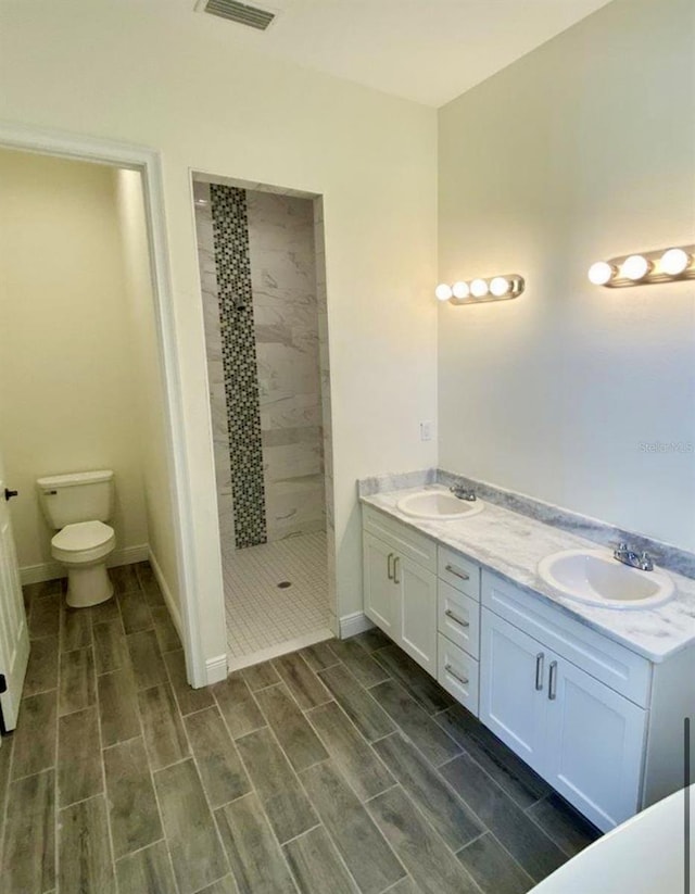 bathroom featuring a tile shower, vanity, and toilet