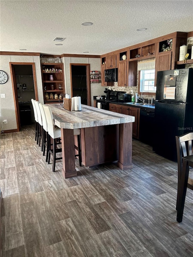 kitchen with a breakfast bar area, black appliances, crown molding, a kitchen island, and a textured ceiling