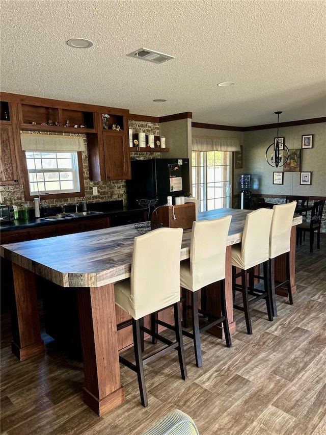 kitchen featuring black refrigerator, a center island, ornamental molding, dark hardwood / wood-style flooring, and decorative light fixtures