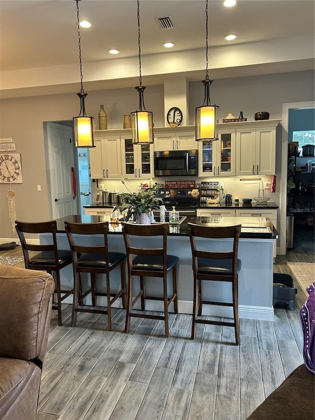 kitchen featuring decorative light fixtures, a kitchen breakfast bar, electric range, and an island with sink