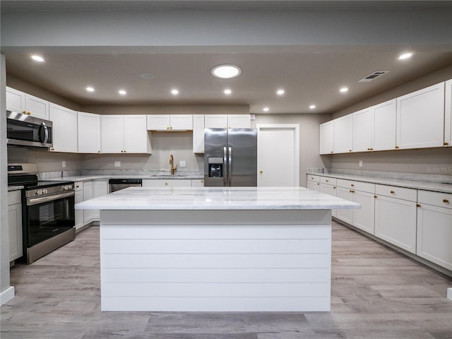 kitchen with light stone countertops, white cabinets, appliances with stainless steel finishes, and a kitchen island