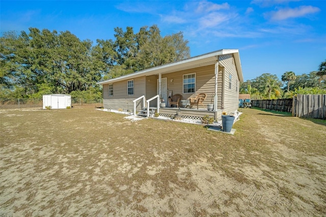 back of house featuring a porch, a yard, and a storage shed