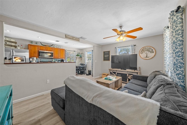 living room featuring light wood-type flooring, ceiling fan, and a textured ceiling