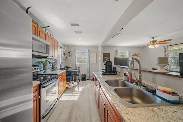 kitchen featuring appliances with stainless steel finishes, ceiling fan, sink, light hardwood / wood-style flooring, and tasteful backsplash