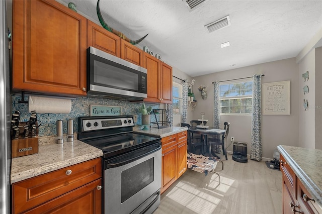 kitchen featuring light stone countertops, a textured ceiling, stainless steel appliances, decorative backsplash, and light wood-type flooring