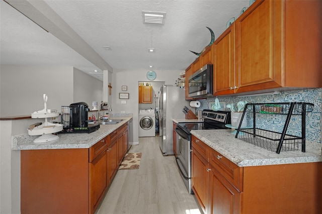 kitchen featuring a textured ceiling, washer / dryer, backsplash, appliances with stainless steel finishes, and sink