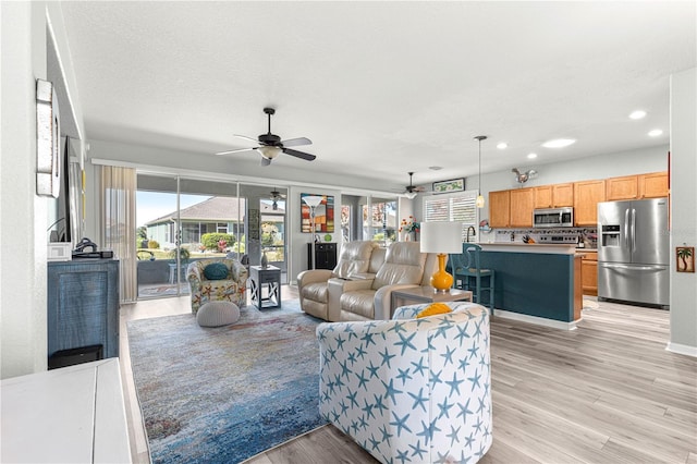 living room with a textured ceiling, ceiling fan, light hardwood / wood-style flooring, and a wealth of natural light