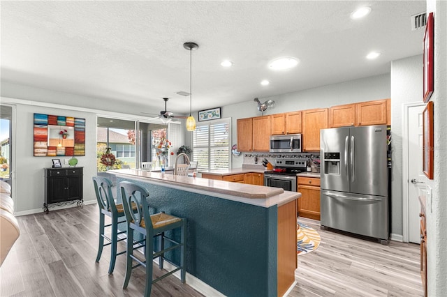 kitchen with light hardwood / wood-style floors, stainless steel appliances, ceiling fan, a kitchen bar, and decorative light fixtures