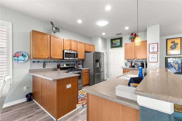 kitchen featuring kitchen peninsula, decorative light fixtures, stainless steel appliances, decorative backsplash, and sink