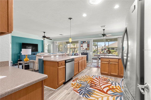 kitchen with a textured ceiling, hanging light fixtures, light hardwood / wood-style floors, a kitchen island with sink, and appliances with stainless steel finishes