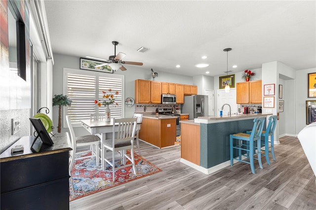 kitchen featuring light wood-type flooring, an island with sink, backsplash, pendant lighting, and appliances with stainless steel finishes