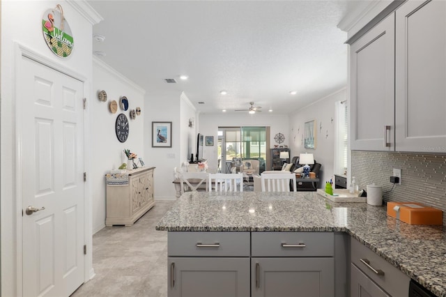 kitchen with gray cabinetry, tasteful backsplash, ornamental molding, kitchen peninsula, and stone counters