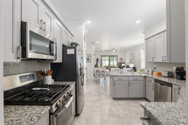 kitchen with decorative backsplash, kitchen peninsula, stainless steel appliances, crown molding, and light stone countertops