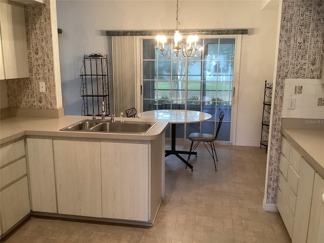 kitchen featuring kitchen peninsula, sink, an inviting chandelier, and pendant lighting