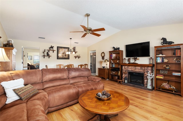 living room with lofted ceiling, ceiling fan, light hardwood / wood-style flooring, and a stone fireplace