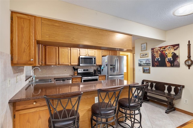 kitchen featuring dark stone countertops, appliances with stainless steel finishes, kitchen peninsula, a kitchen bar, and sink