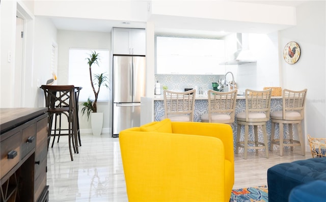 kitchen featuring sink, white cabinetry, stainless steel fridge, and wall chimney exhaust hood