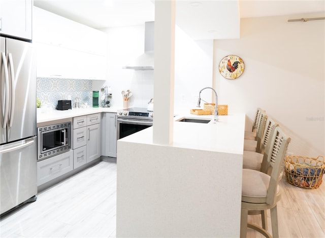 kitchen featuring wall chimney range hood, stainless steel appliances, sink, kitchen peninsula, and a breakfast bar