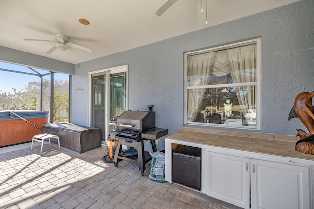 view of patio with glass enclosure, ceiling fan, a hot tub, and a grill